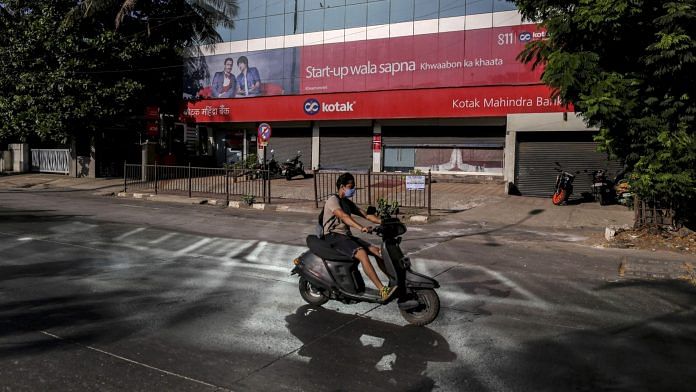 A motorcyclist wearing a protective mask rides past a Kotak Mahindra Bank Ltd. branch on a near-empty street in Mumbai, India. | Photographer: Dhiraj Singh | Bloomberg