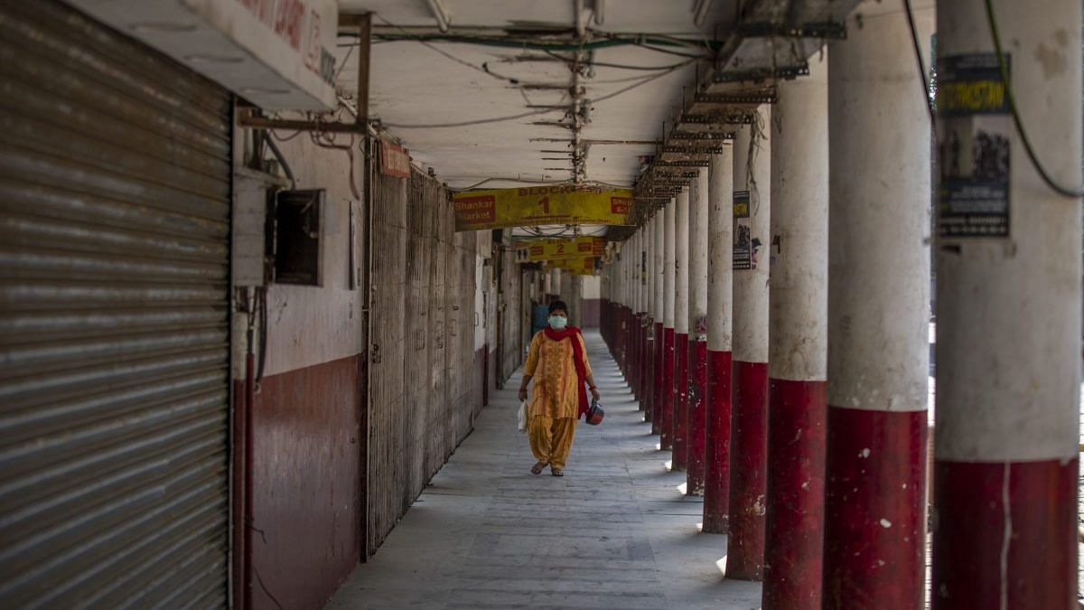 A pedestrian wearing a protective mask walks past shuttered stores in a near-empty Connaught Place during a partial lockdown imposed due to the coronavirus in New Delhi, India | Photographer: Prashanth Vishwanathan | Bloomberg