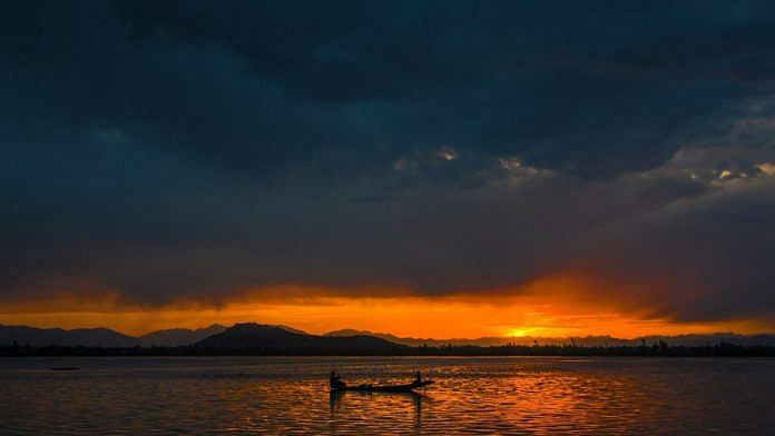A fisherman rows his boat across Dal Lake during sunset, in Srinagar