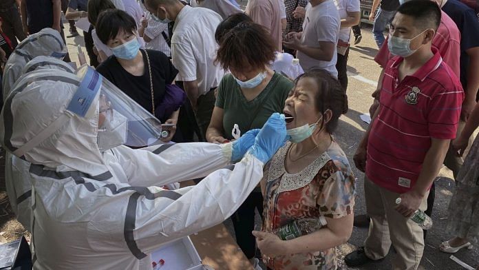 An epidemic control worker conducts a nucleic acid test for Covid-19 on a woman at a testing center in Beijing on 16 June | Bloomberg