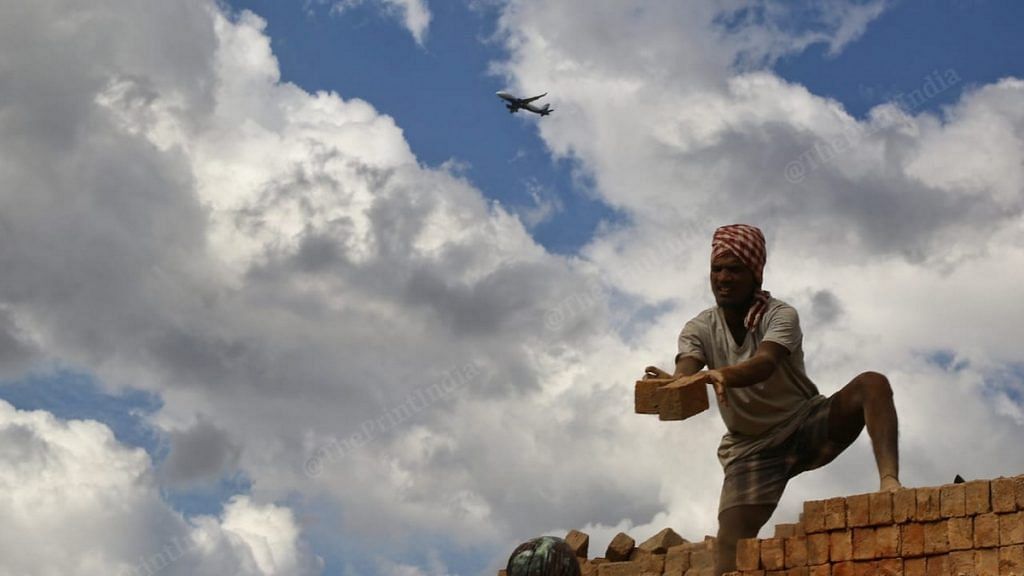 A worker lays bricks in Rangareddy district of Telangana while an airplane passes overhead | Photo: Suraj Singh Bisht | ThePrint