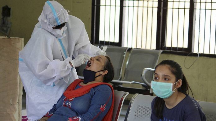 A medic collects swab sample of a woman in Gurugram for a rapid antigen test | PTI