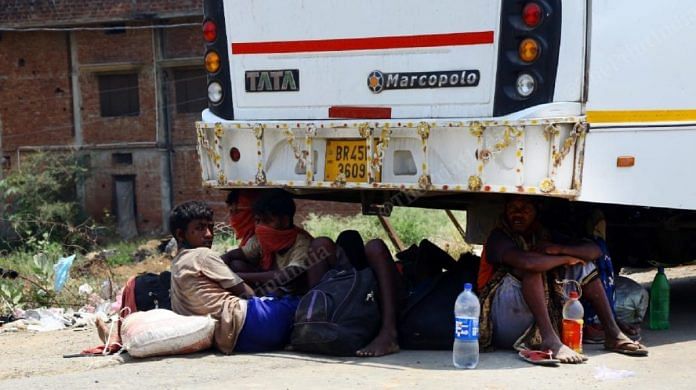 Migrants take a moment of rest under a bus