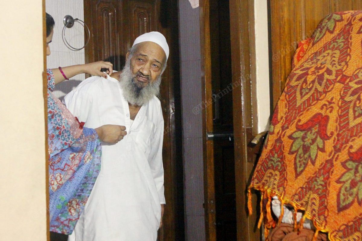 Ahmed does not have his own family, he was adopted by a family in Delhi. Since 13 years he has been living with them. Tayyaba, his grand daughter helps hi wearing the kurta | Photo: Praveen Jain | ThePrint