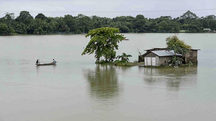 Villagers row a boat near a submerged house to cross a flooded area, in Morigaon district, Assam, 18 July | PTI