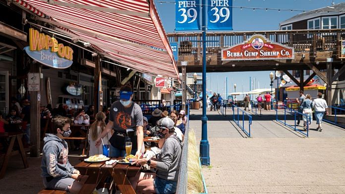 A server wearing a protective mask delivers plates of food at a restaurant on Pier 39 at Fisherman's Wharf in San Francisco, California
