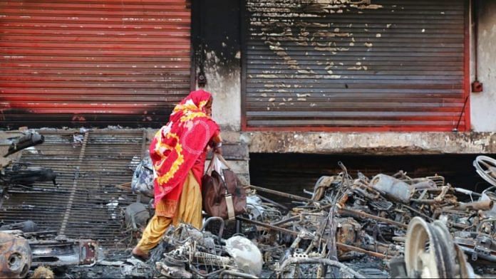 A woman walks through the burnt remains of vehicles set on fire during the Northeast Delhi riots earlier this year | File photo | Suraj Singh Bisht | ThePrint