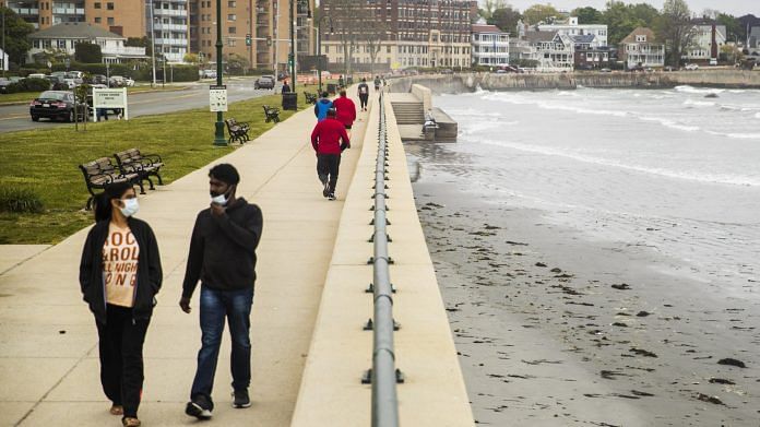 People wearing protective masks walk along the beach in Lynn, Massachusetts on 25 May