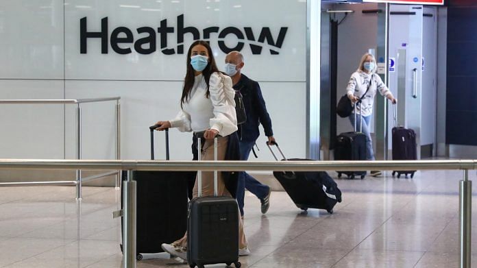 Passengers, wearing protective face masks, walk through the international arrivals hall after arriving at Heathrow Airport in London