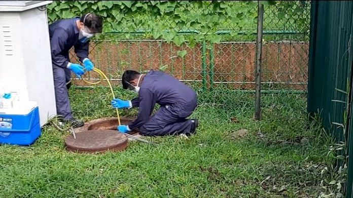 Scientists insert a rubber tube into the manhole outside a foreign workers' dormitory to collect wastewater samples. | Photographer: Faris Mokhtar | Bloomberg