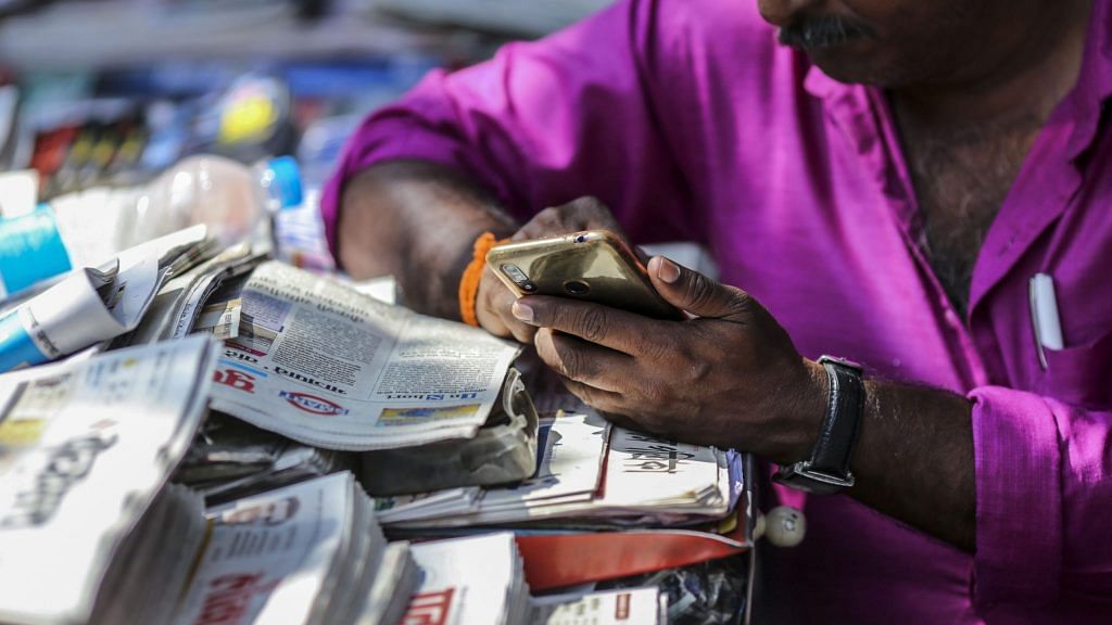 A vendor uses a smartphone while waiting for customers at a newspaper stand in Mumbai, India | Photographer: Dhiraj Singh | Bloomberg