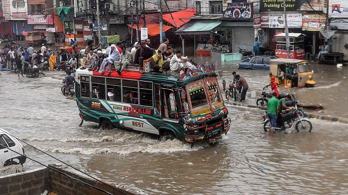 Passengers sit on a bus' roof as the vehicles wades through a flooded street after heavy monsoon rains in Karachi | Photographer: Asif Hassan/AFP/Getty Images via Bloomberg