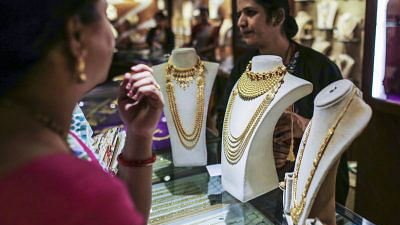 Gold necklaces are displayed on a counter as employees serve customers in Pune
