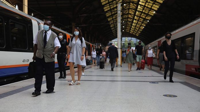 Commuters wearing protective face masks walk along a platform at Liverpool Street railway station, in London on 12 August