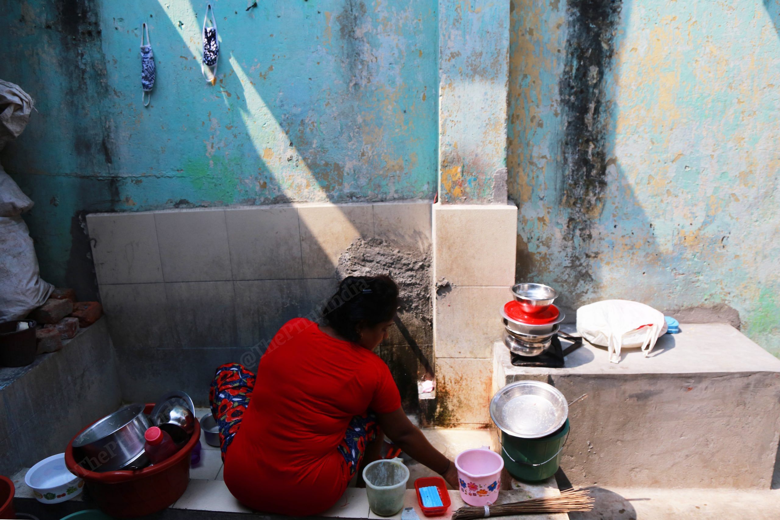 A woman washes utensils at one of the brothels. Also seen, a couple of masks hanging on the wall | Manisha Mondal | ThePrint