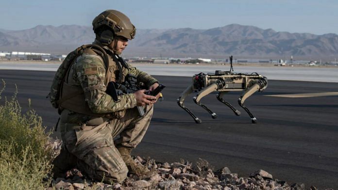 A military man crouches down with him and in front of him is a headless, four-legged robot dog