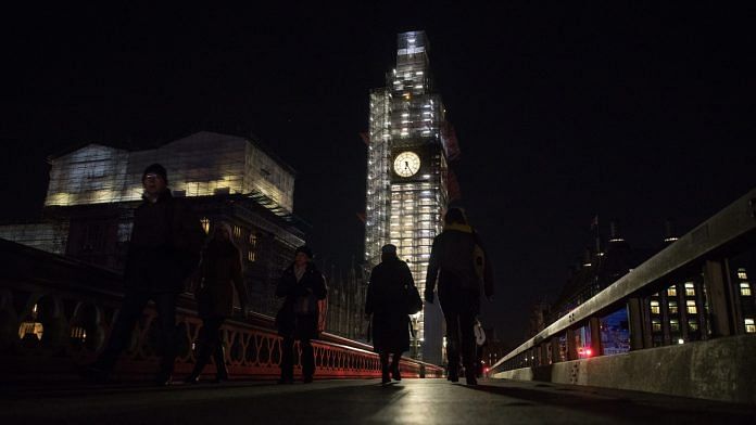 Pedestrians in front of the Elizabeth Tower at the Houses of Parliament at night in London