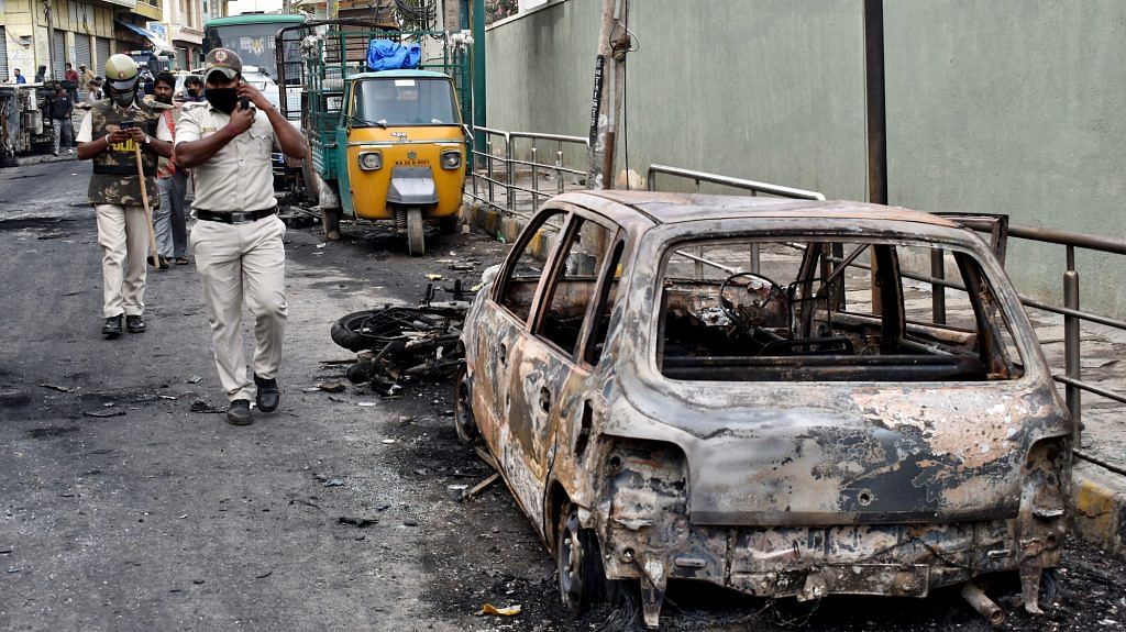 Police personnel pass by vehicles burnt by a mob in Bengaluru on August 12