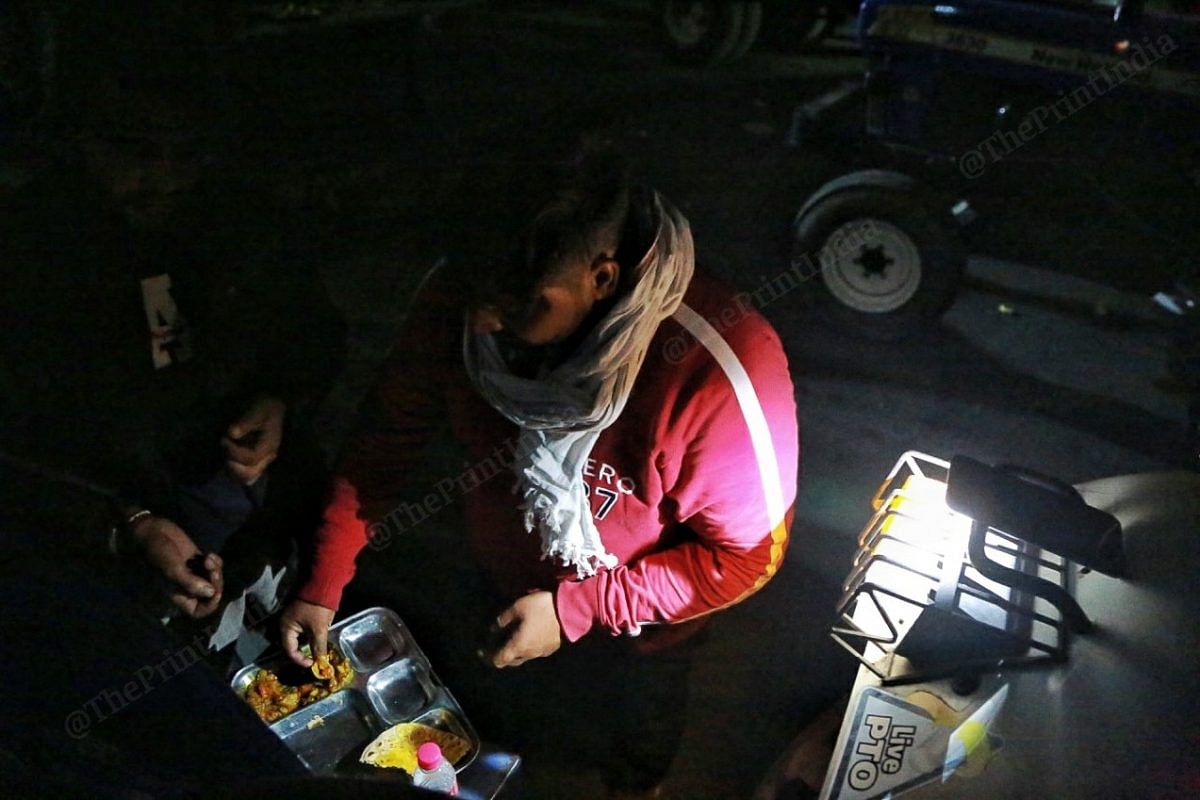 Two men eat dinner with the headlight on of a tractor | Photo: Manisha Mondal | ThePrint
