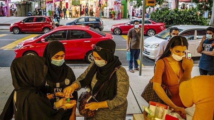 Shoppers use hand sanitizer as a vendor checks a customer's temperature outside a store in Kuala Lumpur, Malaysia | Bloomberg