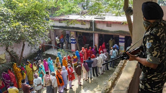 A security official keeps a vigil as voters stand in queues to cast their votes at a polling station during the third phase of Bihar Assembly Elections, at Mahua in Vaishali district, Saturday, Nov. 7, 2020 | PTI