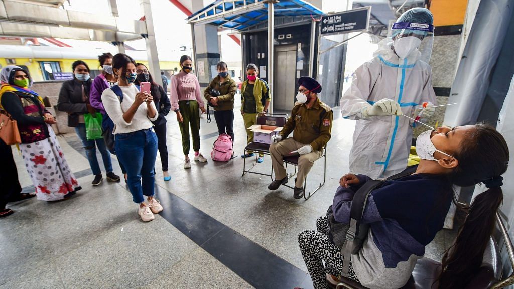 A health worker in protective gear collects a swab sample from a passenger at Nizamuddin Railway Station in New Delhi, on 25 November 2020 | PTI