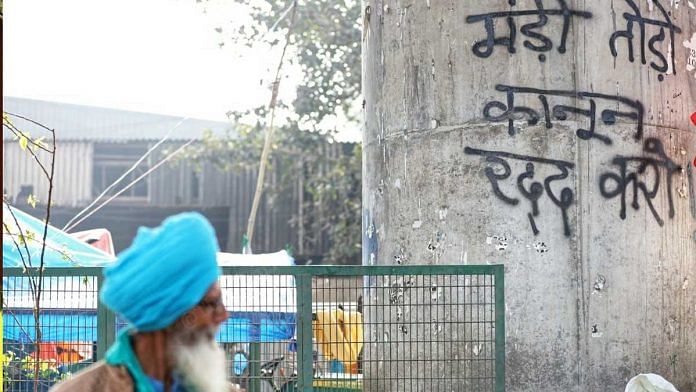 A farmer walks past a sign that reads 'mandi todo kanoon raddh karo' at Tikri border | Photo: Manisha Mondal | ThePrint