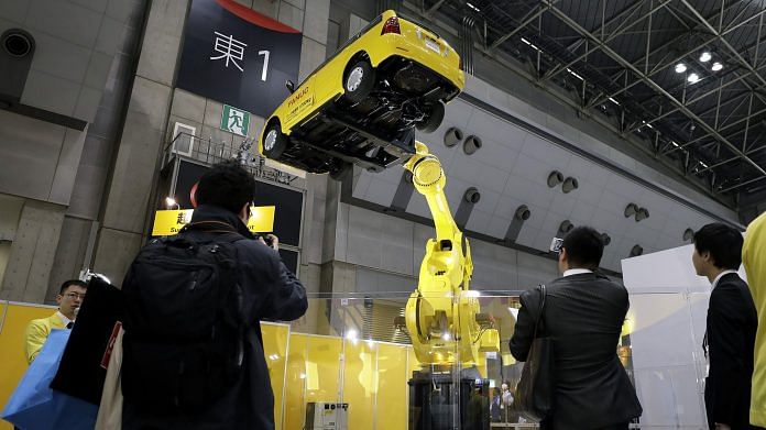 File photo of an industrial robot lifting a vehicle at the International Robot Exhibition in Tokyo, Japan | Image via Bloomberg