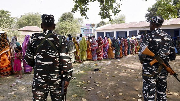 Paramilitary jawans guard as people wait in a queue to cast their votes at a polling station during the first phase of West Bengal Assembly elections, at Chandrapur in Lalgarh, Saturday, March 27, 2021. | PTI
