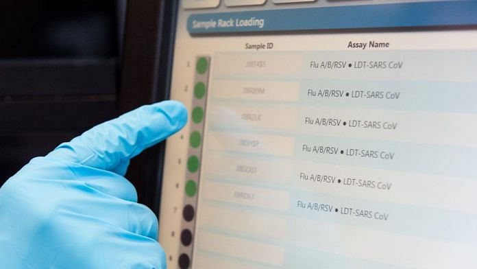 A laboratory worker points to a monitor showing influenza respiratory syncytial virus and coronavirus test information during Covid detection testing | Photo: Geert Vanden Wijngaert | Bloomberg