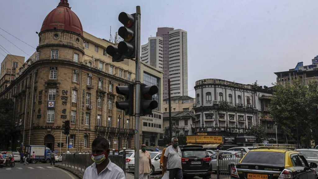 Pedestrians wearing protective masks walk past an out of service traffic signal as the Bombay Stock Exchange (BSE) building stands in the background in Mumbai on 12 October 2020 | Dhiraj Singh | Bloomberg