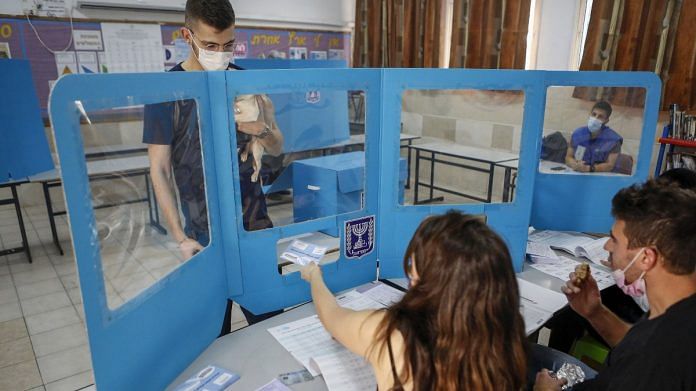 Election officials register a voter from behind a temporary protective shield in Be'er Sheva, Israel, on 23 March 2021 | Photographer: Amnon Gutman | Bloomberg