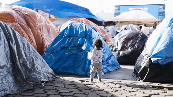 A child walks past tents at a makeshift housing camp for migrants seeking asylum hearings in Tijuana, Mexico | Photographer: Eric Thayer | Bloomberg