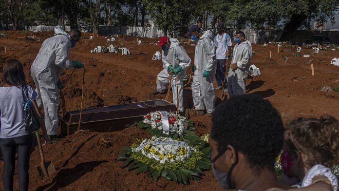 Mourners watch as workers wearing protective equipment bury the casket of a Covid-19 victim at the Vila Formosa cemetery in Sao Paulo, Brazil | Bloomberg