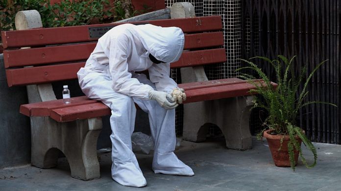 A relative of a Covid-19 fatality wears personal protective equipment (PPE) while sitting on a bench outside a cremation hall at the Nigambodh Ghat crematorium in New Delhi India, on Monday, April 19, 2021. | Photographer: T. Narayan | Bloomberg