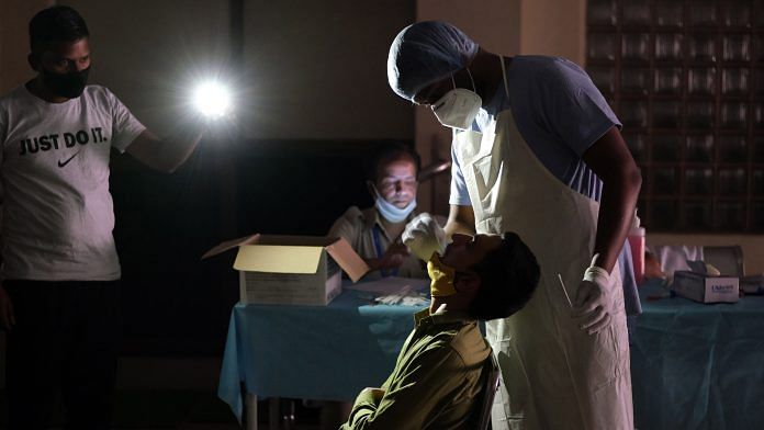 A health worker takes a swab sample under mobile phone torchlight during a power cut at a temporary Covid-19 testing site at the Jawahar Lal Nehru Stadium in New Delhi, on 16 April 2021