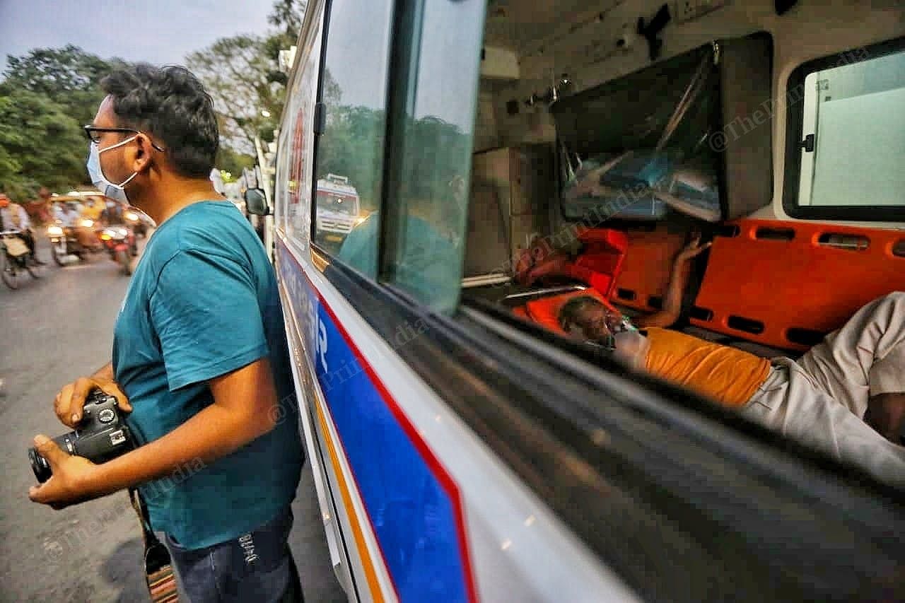 An old man inside lies down inside an ambulance, while a photographer stands outside | Photo: Praveen Jain | ThePrint