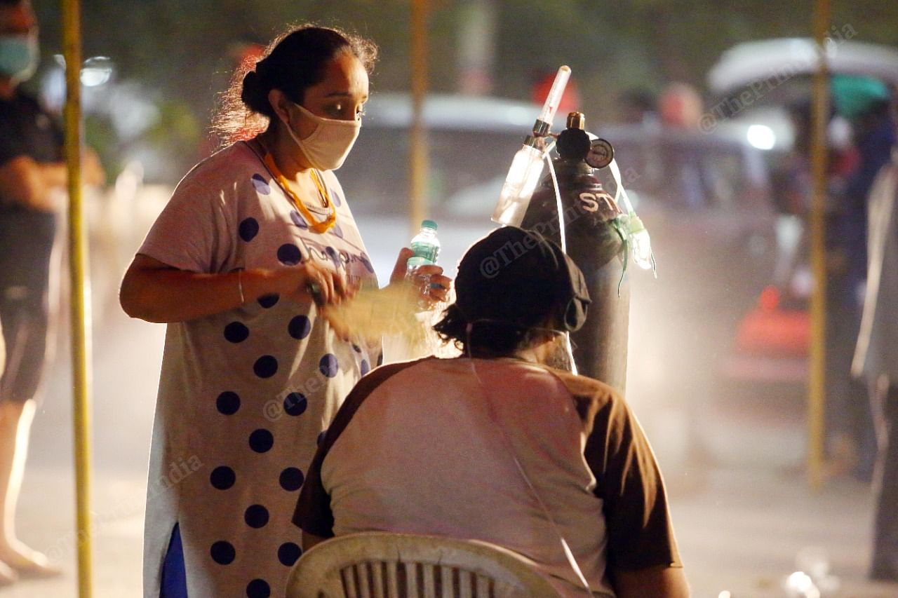 A woman helps a relative attach her mask to an oxygen cylinder outside the Indirapuram Gurudwara |Praveen Jain | ThePrint