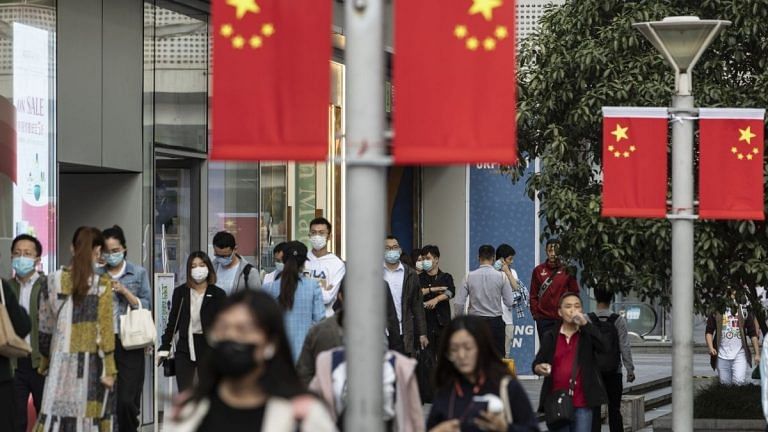 Morning commuters wearing protective masks walk past Chinese flags displayed along Nanjing Road in Shanghai, China | Representational image | Qilai Shen | Bloomberg