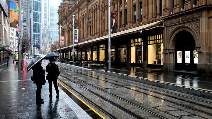 Pedestrians wearing protective masks stand along a near-deserted road during a lockdown in Sydney on 29 June 2021