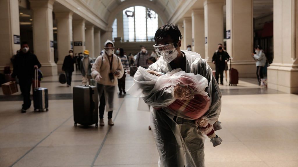 A man carrying a child, both wearing protective masks and raincoats, walk inside the Hankou railway station in Wuhan, China | Representational image | Bloomberg