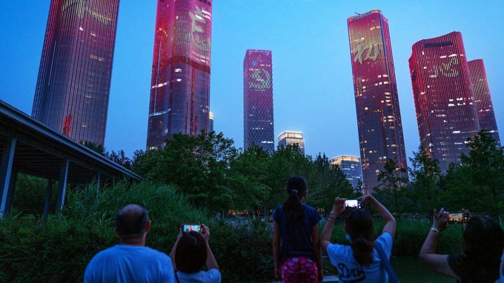 Chinese characters reading 'Never forget the original intention' and the emblem of the Chinese Communist Party illuminate buildings during a light show in Beijing, on 26 June 2021 | Bloomberg
