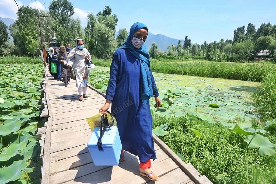Medical team with Asha workers crossing a pool while they go for door to door vaccination drive in Srinagar's Abidal | Photo: Praveen Jain | ThePrint