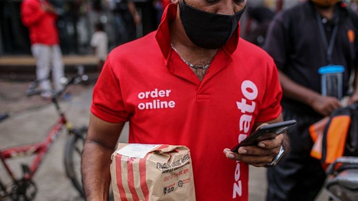 Zomato delivery rider looks at a smartphone while carrying an order in Mumbai | Representational image | Bloomberg