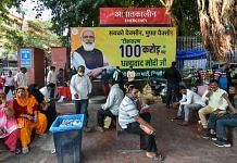 People sit near a poster commemorating India's 1 billion Covid-19 vaccine dose milestone at RML Hospital in New Delhi, on 21 October 2021 | PTI
