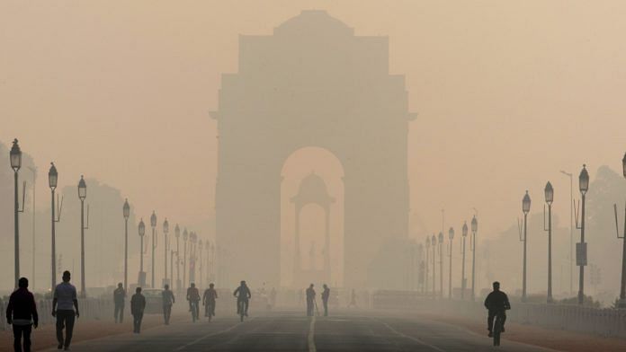 Pedestrians walk along Rajpath boulevard as India Gate monument stands shrouded in smog in New Delhi, India| Bloomberg