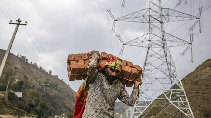 A worker carries a bundle of bricks on his back past a Sterlite Power Transmission Ltd. transmission tower in J&K's Rajouri district (representational image) | Photographer: Dhiraj Singh | Bloomberg
