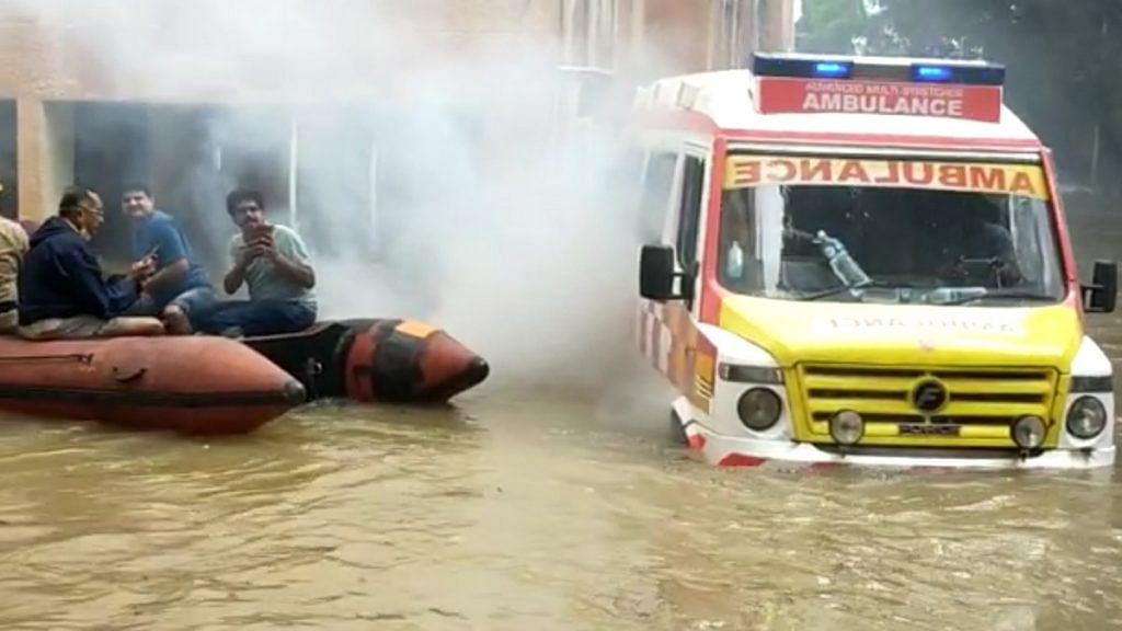 An ambulance makes its way through the waterlogged streets of Bengaluru beside an inflatable boat | By special arrangement