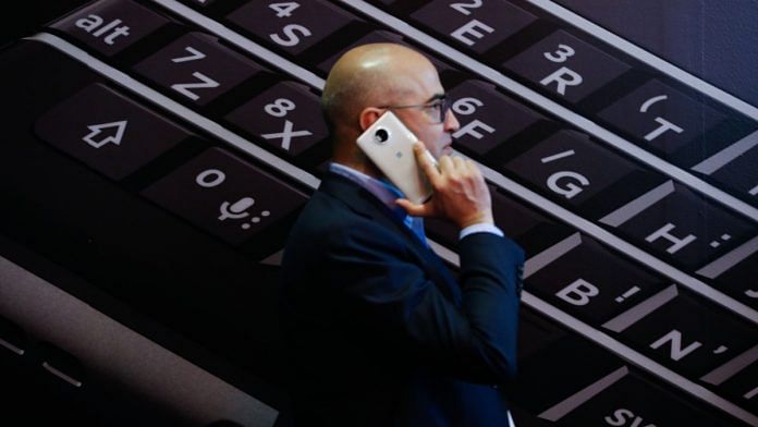 An attendee uses his mobile device as he walks past a poster for the Blackberry Keyone smart phone in Barcelona, Spain | Representational image | Bloomberg