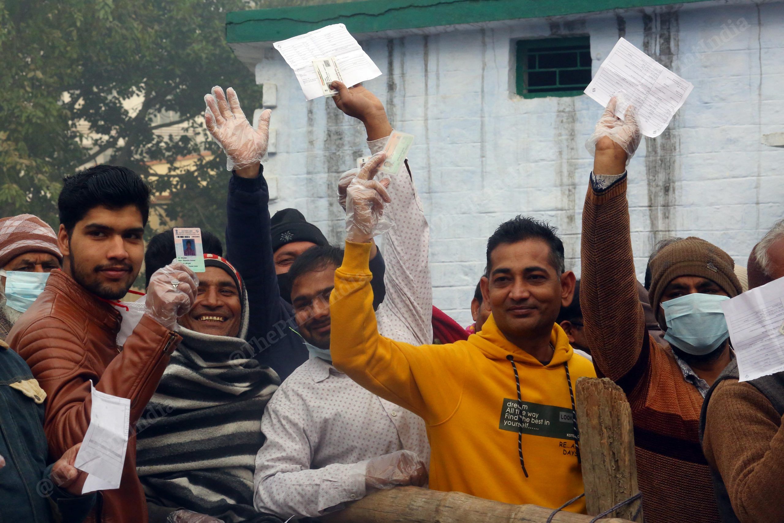 People hold up their identification documents as they wait to cast their votes in the the first phase of 2022 UP Assembly elections | Praveen Jain | ThePrint
